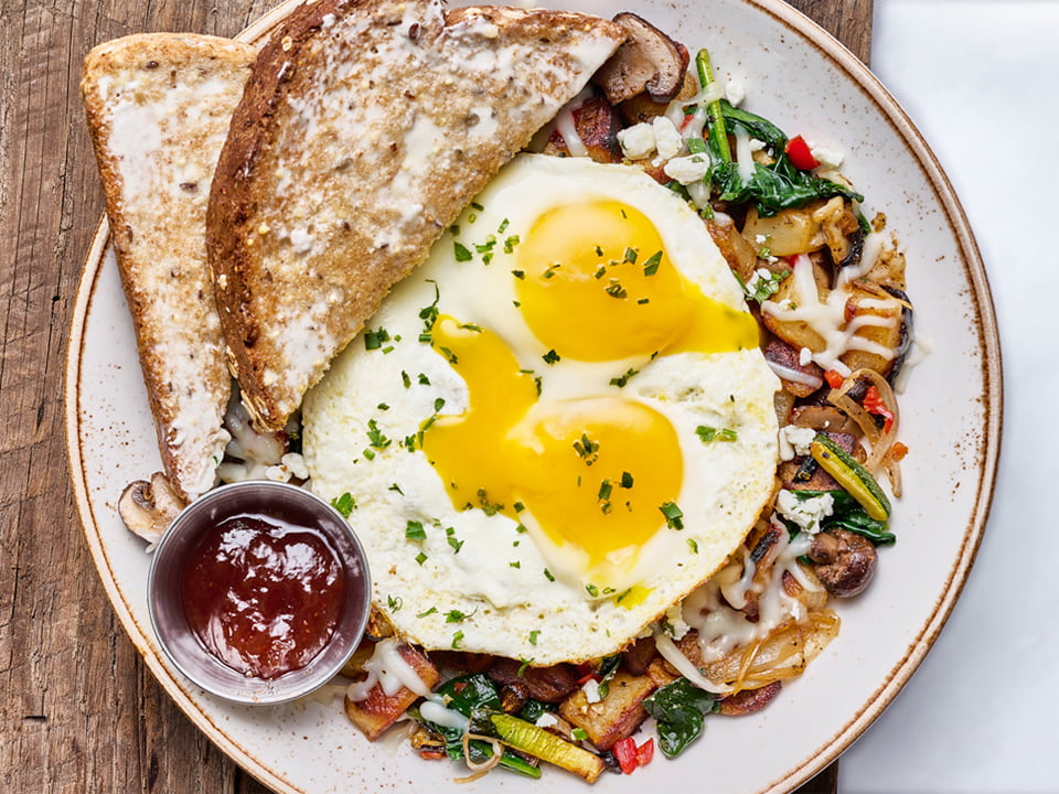 Two cage-free eggs any style atop fresh, seasoned potatoes, house-roasted Crimini mushrooms, zucchini, shallots, red peppers, baby spinach, melted Mozzarella and herbed Goat cheese. Served with our whole grain artisan toast.