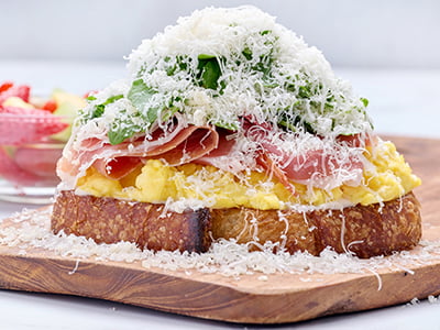 Thick-cut, griddled artisan sourdough topped with thinly shaved prosciutto, scrambled cage-free eggs, Monterey Jack, freshly grated Parmesan, lemon-dressed arugula and roasted garlic aioli. Served with a cup of fresh fruit.
