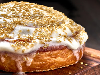 A freshly baked cinnamon roll glazed with lemon cream cheese frosting and gilded with luxurious gold sprinkles.