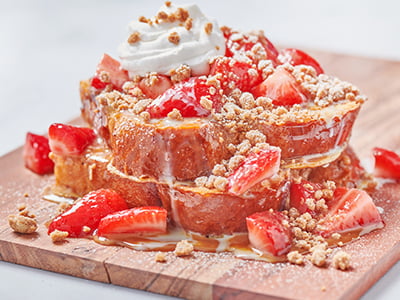 Thick-cut, custard-dipped challah bread griddled and topped with fresh strawberries, sweetened condensed milk, warm dulce de leche, whipped cream and spiced gingerbread cookie crumbles and lightly dusted with powdered cinnamon sugar.