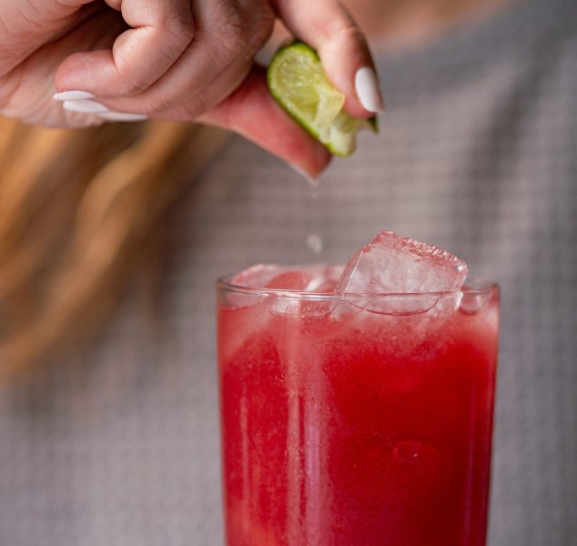 A woman squeezing lime juice into a glass of Pomegranate Pear Punch.