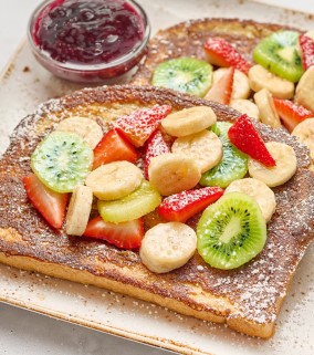 A plate with slices of Floridian French Toast topped with fresh bananas, strawberries and kiwifruit.