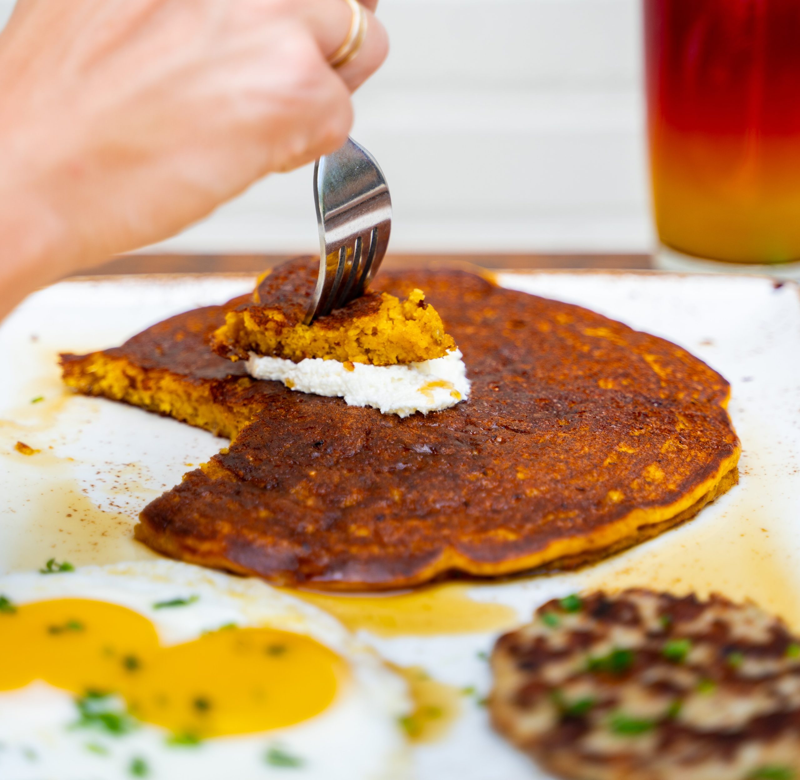 A plate with a pumpkin pancake, fried eggs and sausage patty.